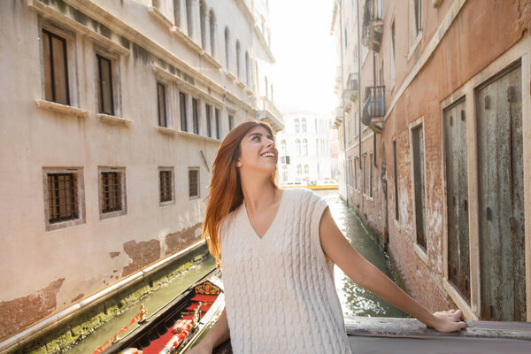 happy redhead woman in summer knitwear looking at medieval buildings in Venice