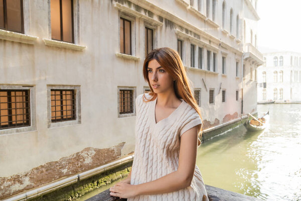 young woman in sleeveless jumper standing near building over urban canal in Venice
