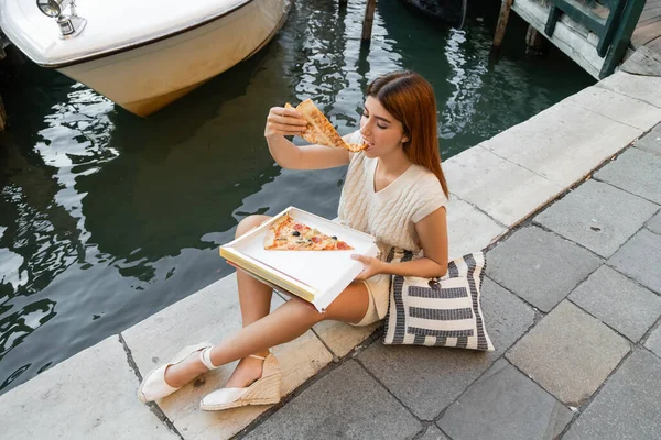 Venedik tatili sırasında çantalı ve lezzetli pizzanın tadını çıkaran kadının yüksek açılı görüntüsü