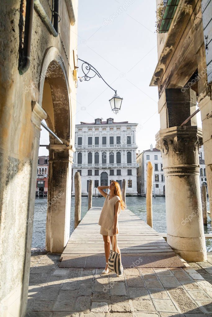 full length of young woman with striped bag near ancient buildings and Grand Canal in Venice