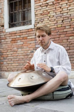 Barefoot musician playing metal hang on urban street in Venice 