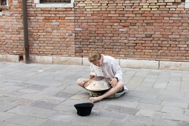 Street musician playing handpan near hat on sidewalk in Venice 