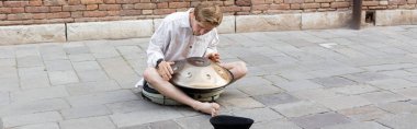 Musician playing hang near hat on sidewalk in Venice, banner 