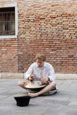 Musician playing hang drum near hat on urban street in Venice 