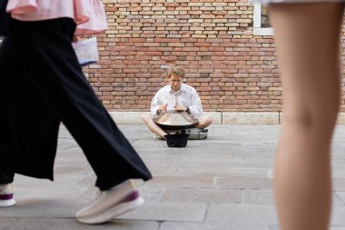 Musician playing hang drum near hat on urban street in Venice 