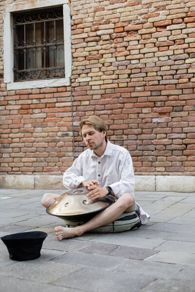 Босоногий музыкант с закрытыми глазами играет на сковородке на городской улице в Венеции 