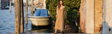 Young pregnant woman in dress standing on pier in Venice, banner 