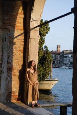 Cheerful pregnant woman standing in arch near pier in Venice 