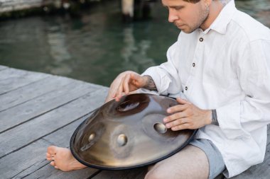Barefoot musician playing metal hang drum on pier in Venice 