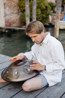 Tattooed musician playing handpan on pier in Italy 