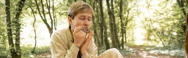 Musician playing jews harp in blurred summer forest, banner 
