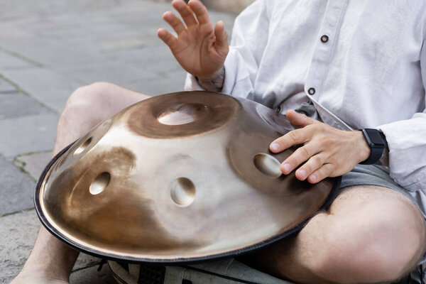 Обрезанный вид уличного музыканта, исполняющего висячий барабан на городской улице 