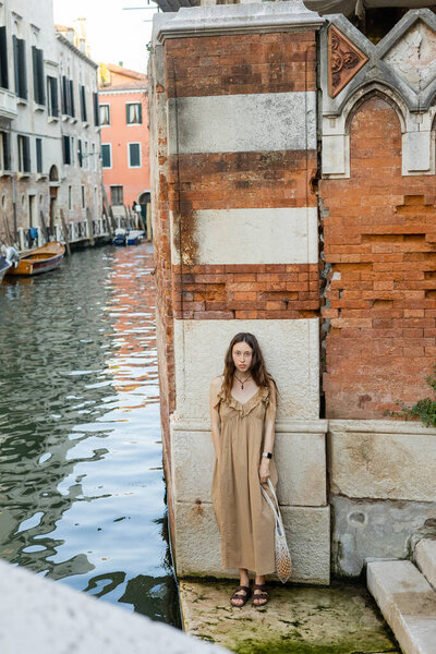 Young woman in dress looking at camera near old building in Venice 