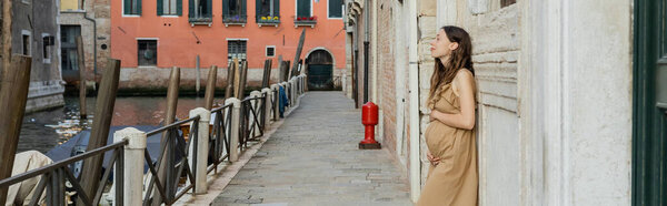 Side view of pregnant woman looking at river on urban street in Venice, banner 