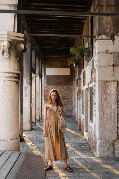 Pregnant woman holding string bag near old building in Venice