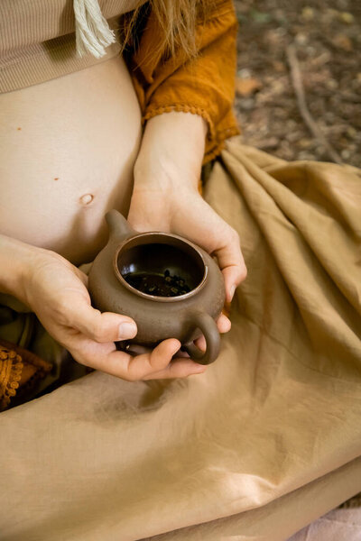 Cropped view of pregnant woman holding teapot in forest 