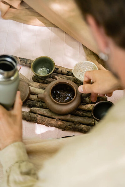 Cropped view of blurred man holding thermos and teapot on blanket outdoors 