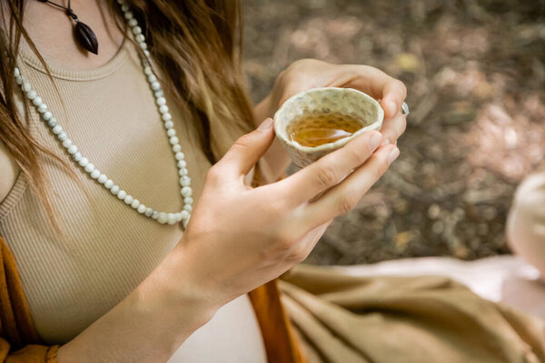 Cropped view of pregnant woman holding bowl with tea in forest 
