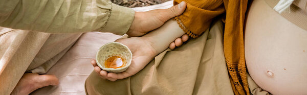 Cropped view of man touching pregnant wife during tea ceremony in forest, banner 