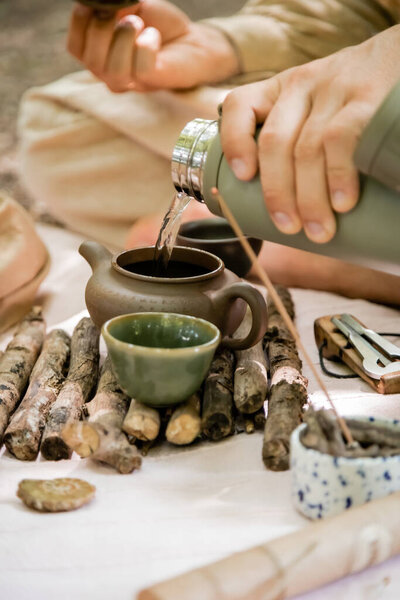 Cropped view of man pouring hot water in teapot during tea ceremony in forest 