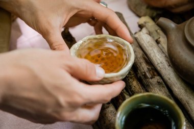 Cropped view of woman holding bowl near wooden board during tea ceremony outdoors 