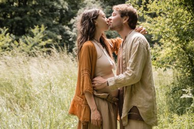 Side view of pregnant woman kissing husband in forest 