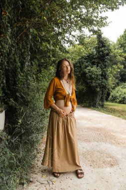 Pregnant woman standing on walkway near tree in forest 
