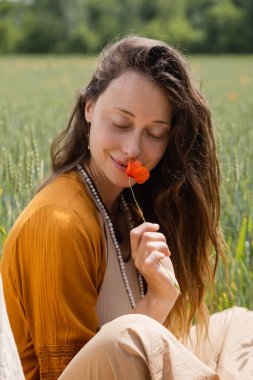 Smiling young woman smelling poppy flower in field  clipart