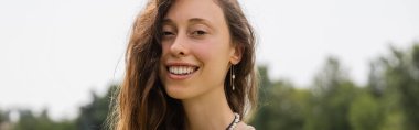 Cheerful brunette woman looking at camera outdoors, banner 