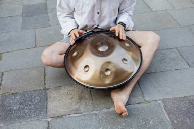 Cropped view of barefoot musician playing hang on sidewalk outdoors 