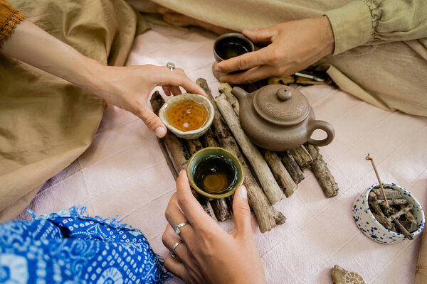 Cropped view of friends holding bowls with tea on wooden board outdoors 
