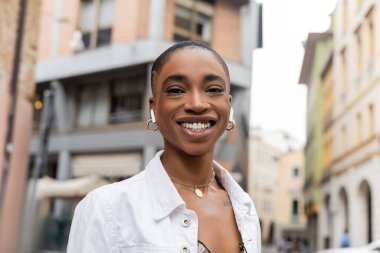 Kısa saçlı ve kulaklıklı neşeli Afro-Amerikalı kadın Treviso 'da kameraya bakıyor.