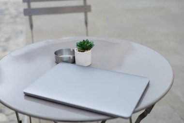 Laptop near plant and ashtray on bistro table outdoors  clipart