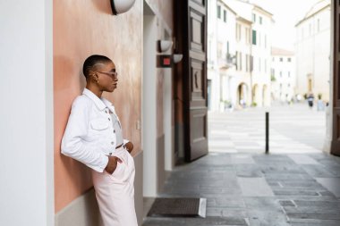 Treviso 'daki şehir caddesinde güneş gözlüklü, şık Afro-Amerikalı bir kadının yan görüntüsü.