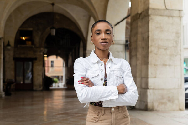 Short haired african american tourist crossing arms and looking at camera on blurred urban street in Treviso