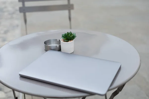 Laptop near plant and ashtray on bistro table outdoors