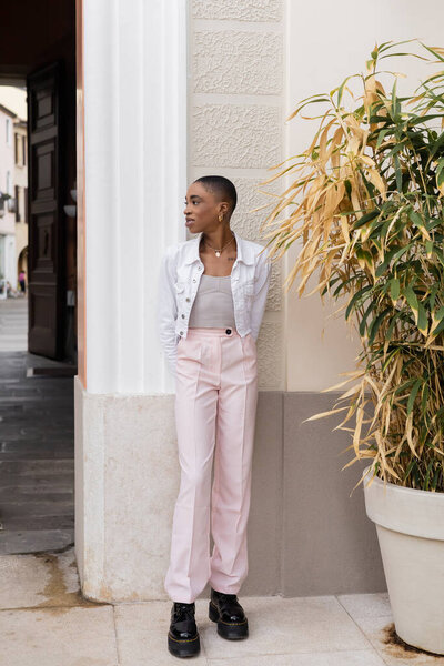 Trendy african american woman standing near plant and building on street in Treviso