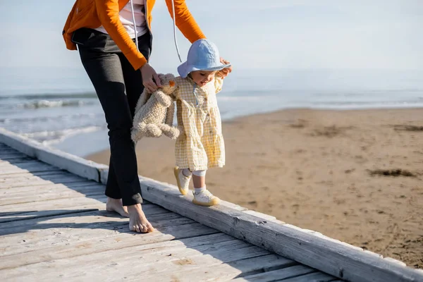 Maman tenant jouet tandis que bébé fille marche sur la plage en Italie — Photo de stock