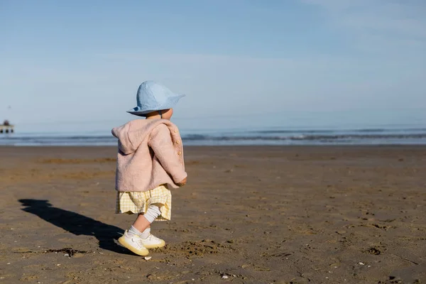 Bébé fille en veste et chapeau panama marche sur la plage en Italie — Photo de stock