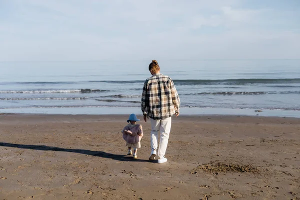 Vista trasera de padre e hija pequeña caminando en la playa de arena cerca del mar adriático en Italia — Stock Photo