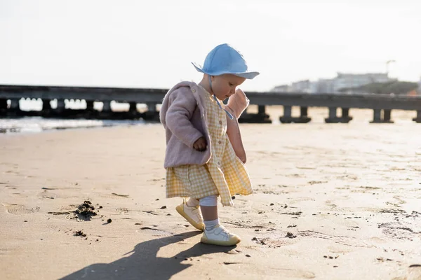 Vista laterale della bambina in cappello panama che cammina sulla spiaggia in Italia — Foto stock