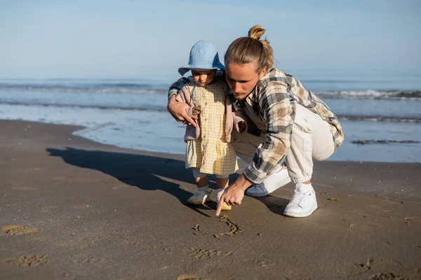 Homem desenhando na areia perto da filha da criança na praia na Itália — Fotografia de Stock