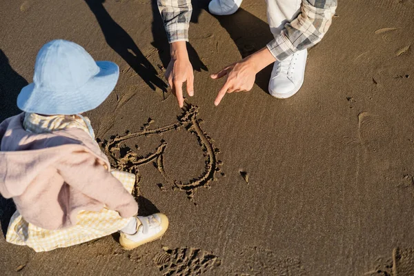 Чоловік вказує на знак серця на пісок поруч з дівчинкою на пляжі — стокове фото