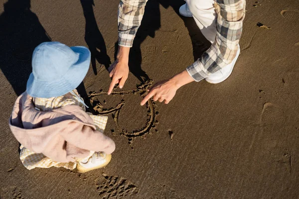 Vue grand angle de l'homme dessinant signe de coeur sur le sable près de la fille tout-petit — Photo de stock