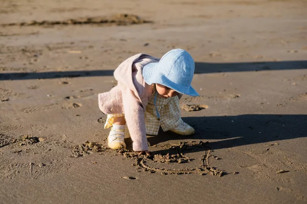 Enfant en bas âge en chapeau panama dessin signe du coeur sur la plage — Photo de stock
