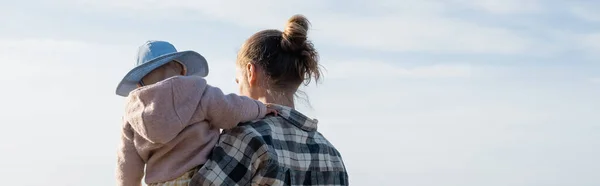 Young man holding baby with blue sky at background, banner — Stock Photo