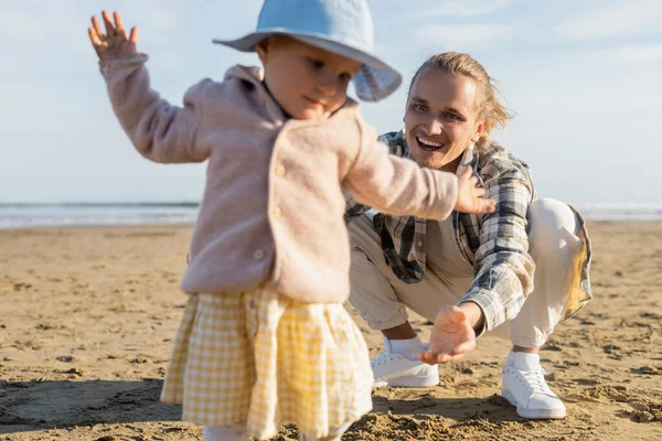 Улыбающийся мужчина смотрит на размытую маленькую дочь на пляже в Италии — стоковое фото