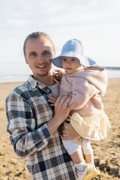 Young father holding baby and looking at camera on beach in Italy — Stock Photo