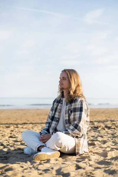 Hombre de pelo largo meditando en la playa en Italia - foto de stock