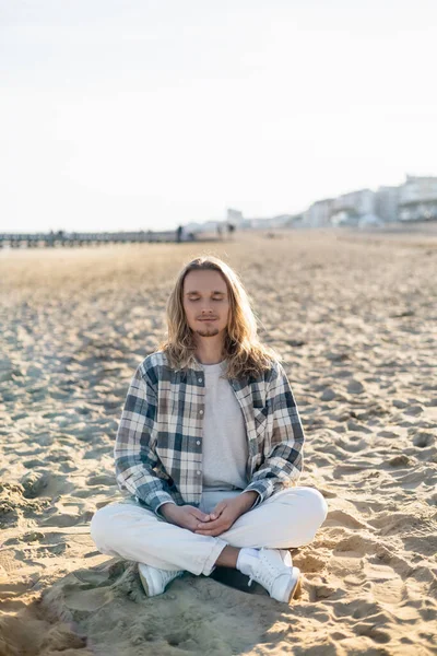 Joven con los ojos cerrados meditando en la playa en Italia - foto de stock